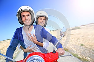 Cheerful couple riding moto in desertic island