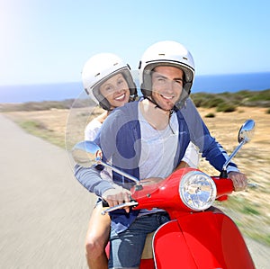 Cheerful couple riding scooter by the seaside