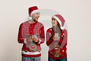 Cheerful Couple In Santa Hats Holding Smartphones And Looking At Each Other