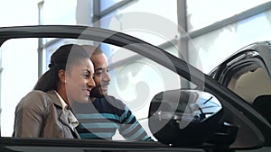 Cheerful couple showing thumbs up while examining a new car