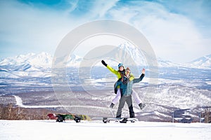 Cheerful couple with snowboards in front of snowy volcanos