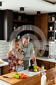 Cheerful couple stands in a well-lit kitchen, engrossed in a digital tablet among fresh ingredients