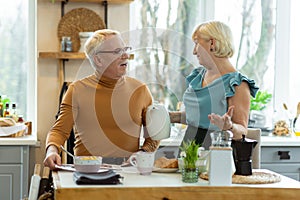 Cheerful couple talking during breakfast while sitting at the kitchen