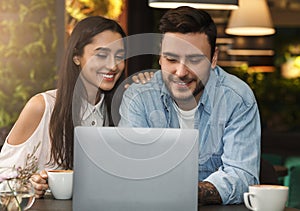 Cheerful Couple Using Laptop Having Coffee Sitting In Cafe