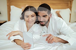 Cheerful Couple Using Smartphone Lying In Bed In Hotel Indoors