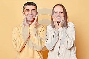 Cheerful couple woman and man wearing casual style clothing standing isolated over beige background smiling to camera keeping