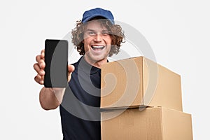 Cheerful courier with boxes showing smartphone