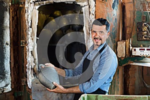 Cheerful craftsman carrying fresh baked black glazed vessel