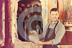 Cheerful craftsman carrying fresh baked black glazed vessel