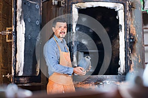 Cheerful craftsman carrying fresh baked black glazed vessel