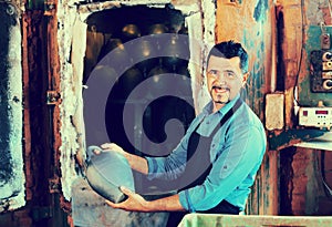 Cheerful craftsman carrying fresh baked black glazed vessel