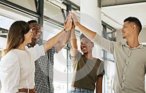 Cheerful creative business team standing in office and giving high five while celebrating a win. Diverse business people