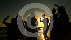 Cheerful crowd dancing on the beach. They jump in the sun. People are having fun. They are happy. Silhouettes of people