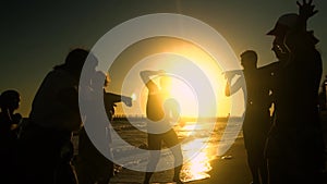 Cheerful crowd dancing on the beach. They jump in the sun. People are having fun. They are happy. Silhouettes of people