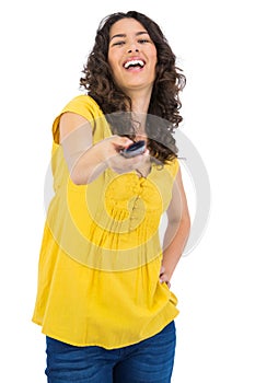Cheerful curly haired pretty woman changing channel with remote