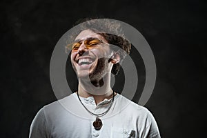 Cheerful and curly man wearing sunglasses posing in the dark studio