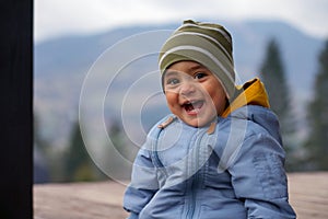 Cheerful cute baby boy laughing while sitting outdoor - happy adorable toddler smiling outdoors