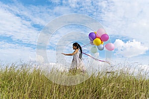 Cheerful cute girl holding balloons running on green meadow white cloud and blue sky with happiness. Hands holding vibrant air