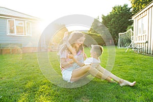 Cheerful cute preschooler boy kid having fun with his mum, embracing, laughing on the green grass. Young mom and kid