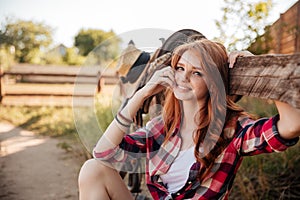 Cheerful cute redhead cowgirl resting at the ranch fence