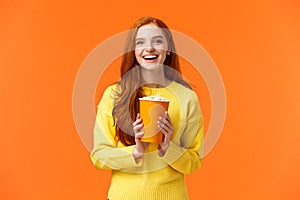 Cheerful cute redhead curly girlfriend holding popcorn chat with boyfriend before movie start at cinema, smiling