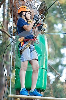 Cheerful cute young boy in blue t shirt and orange helmet in adventure rope park at sunny summer day. Active lifestyle, sport