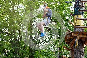 Cheerful cute young boy in blue t shirt and orange helmet in adventure rope park at sunny summer day. Active lifestyle, sport