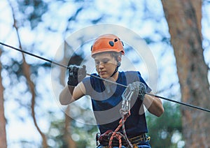 Cheerful cute young boy in blue t shirt and orange helmet in adventure rope park at sunny summer day. Active lifestyle, sport,