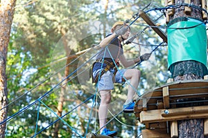 Cheerful cute young boy in blue t shirt and orange helmet in adventure rope park at sunny summer day. Active lifestyle, sport