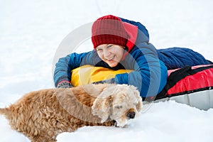 Cheerful cute young boy in orange hat red scarf and blue jacket holds tube on snow, has fun, smiles. Teenager on sledding