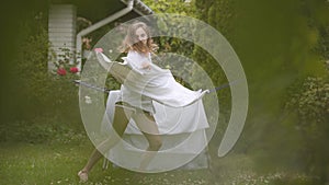 Cheerful cute young woman have fun singing and dancing at the backyard while doing house work with the linen. Washday