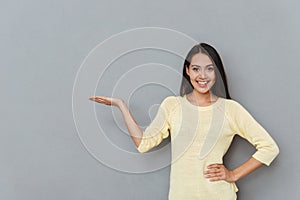 Cheerful cute young woman standing and holding copyspace on palm
