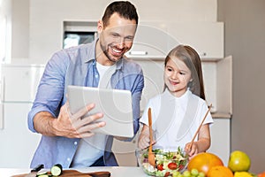 Cheerful Dad And Daughter Cooking Using Digital Tablet In Kitchen