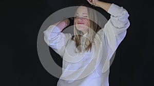 Cheerful dance of a girl in a white hoodie in a dark room, A woman with a carefree expression dancing in a white hoodie