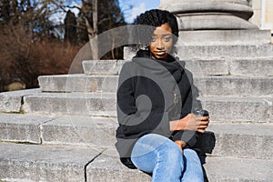 Cheerful dark skinned woman enjoying coffee holding to go cup recreating in city park, happy trendy dressed african american