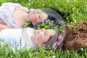 Cheerful daughter resting on meadow with mom