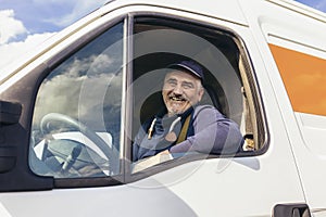 Cheerful delivery driver looking out the window of the white cargo van vehicle, delivering goods by car