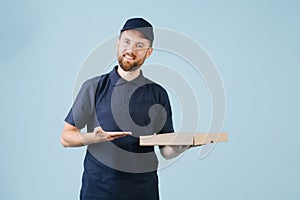 Cheerful delivery man in uniform is holding cardboard pizza box