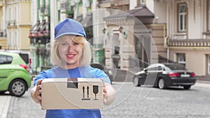 Cheerful delivery woman in blue uniform holding cardboard box