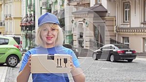 Cheerful delivery woman in blue uniform holding cardboard box
