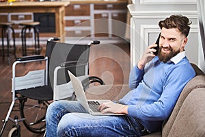 Cheerful disabled businessman sitting on a couch, working on a laptop