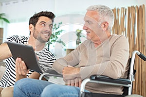 cheerful disabled retired man sitting in wheelchair near bearded son photo