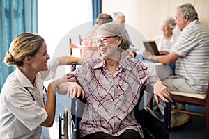 Cheerful disabled senior woman sitting on wheelchair looking at female doctor