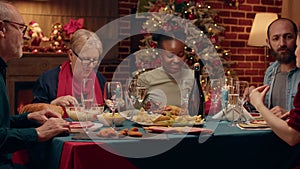 Cheerful diverse family enjoying Christmas dinner inside cozy Xmas decorated apartment