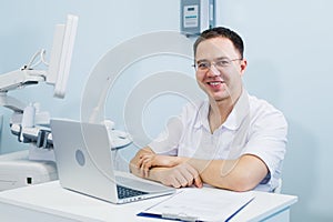 Cheerful doctor sitting at doctor`s office with laptop