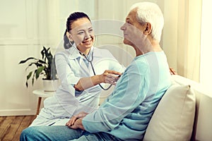 Cheerful doctor using stethoscope for checking lungs of elderly man