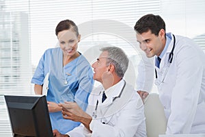 Cheerful doctors and surgeon working together on computer