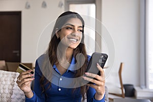 Cheerful dreamy young Indian consumer woman enjoying online shopping