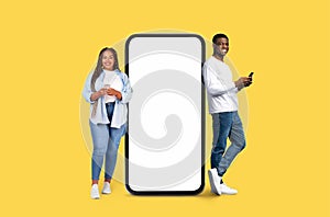 Cheerful duo next to smartphone mockup on yellow