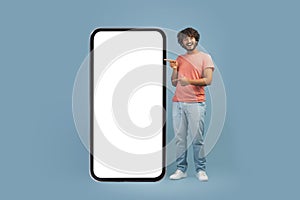 Cheerful eastern guy pointing at big smartphone with empty screen